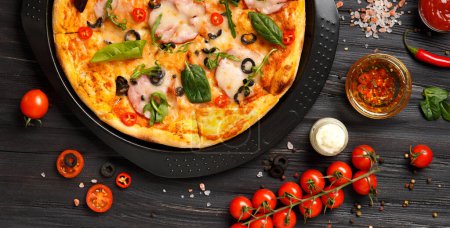 Téléchargez les photos : Pizza avec saccades, olives, fromage et herbes sur un plat rond noir, tomates cerises fraîches, sauces et épices sur fond bois foncé, vue sur le dessus - en image libre de droit