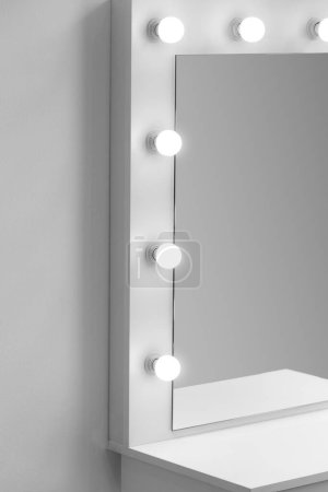 Foto de Parte de un tocador blanco moderno con un gran espejo y lámparas brillantes contra una pared blanca, primer plano, espacio para el texto. Lugar de trabajo del maquillador, vestidor - Imagen libre de derechos