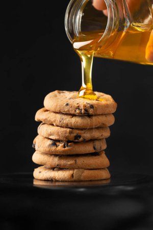 Photo for Honey pours on homemade cookies with pieces of chocolate on a dark background close -up. A composition of craft cookies and pouring honey. - Royalty Free Image