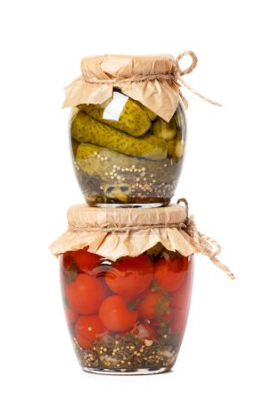 Foto de Tomates y pepinos en escabeche en dos frascos uno encima del otro, aislados sobre un fondo blanco. Calabazas enlatadas y tomates cherry. - Imagen libre de derechos