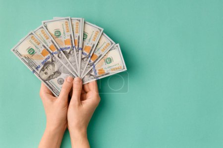 Photo for A lot of bills of 100 dollars in hands are folded in a fan on a green background top view with space for text. Currency, banknotes in female hands. The concept of success, business, wealth. - Royalty Free Image
