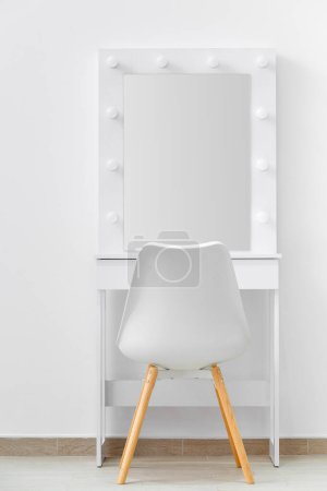 Téléchargez les photos : Table de toilette blanche pour le maquillage avec un grand miroir et des lampes, une chaise blanche sur le fond du mur. Maquilleur lieu de travail, dressing moderne. - en image libre de droit