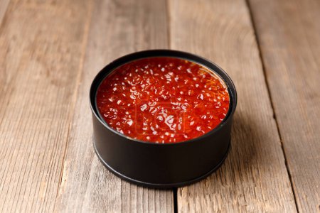Photo for Red salmon caviar in an open black tin can on wooden background. Useful delicacy seafood, canned fish. - Royalty Free Image
