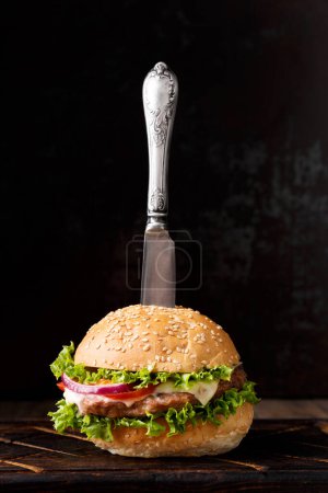 Téléchargez les photos : Hamburger frais appétissant au boeuf sur fond sombre, couteau vintage dans un hamburger. - en image libre de droit