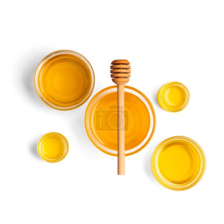 Téléchargez les photos : Composition créative de miel dans des bols en verre de différentes tailles et une trempette en bois sur fond blanc vue de dessus. Miel biologique et cuillère à miel sur l'isolement. - en image libre de droit