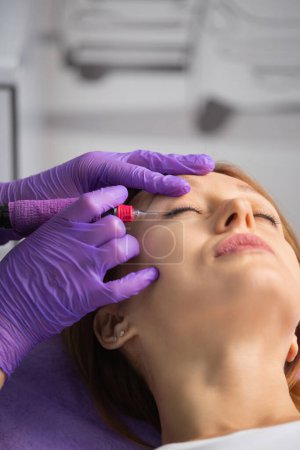 Photo for A beauty artist performs permanent makeup on a girl's upper eyelids. Interlash tattoo. Arrow tattoo on the upper eyelid. - Royalty Free Image