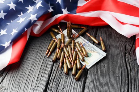 Amerikanische Flagge, Dollars, Kugeln, Granaten, Patronen, Munition auf schwarzem Holzgrund. Das Konzept der Kreditvergabe, der Armee, des Waffenverkaufs. Rüstungsindustrie, Krieg, weltweiter Waffenhandel.