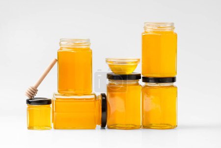 Téléchargez les photos : Composition conceptuelle de bocaux en verre sous forme de nids d'abeilles avec du miel et une trempette en bois sur fond blanc. Composition créative de pots de miel fermés et ouverts les uns sur les autres. - en image libre de droit