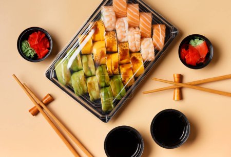 Téléchargez les photos : Un ensemble de rouleaux de sushi multicolores lumineux avec crevettes, saumon, avocat dans un emballage en plastique, baguettes chinoises, sauce, gingembre sur un fond clair, vue sur le dessus. Livraison de sushi - en image libre de droit