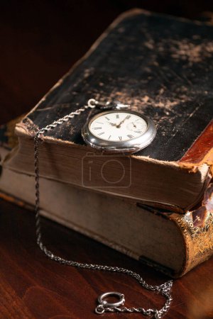 Round old clock with an iron chain on an ancient book close-up