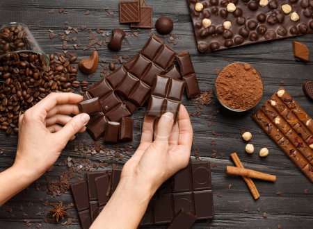 Photo for Chocolate in female hands, chocolate bars, sweets, cocoa powder, coffee, spices, hazelnuts on a dark wooden background. The concept of confectionery, variety of chocolate. - Royalty Free Image