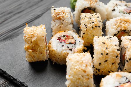 Téléchargez les photos : Ensemble de rouleaux de sushi au saumon, caviar, graines de sésame sur une plaque d'ardoise en pierre noire, gros plan. - en image libre de droit