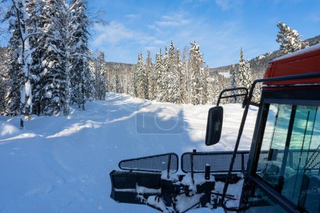 red snowcat rides in a snowy spruce forest, view from the cab. Freeride trip for skiers and snowboarders. Blue sky. Winter activities, adventures, travel. High quality photo