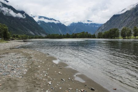 sand and stone river bank surrounded by mountains in the clouds. High quality photo