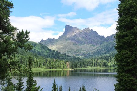 Orilla del gran lago de montaña Svetloye y pico Zvezdnyy rodeado de bosques de coníferas verdes, en el parque natural Ergaki. Paisaje de verano con buen tiempo. Lugar para el alpinismo, senderismo, viajes