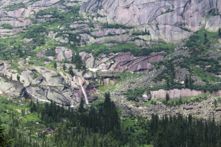 Kleiner Wasserfall im Naturpark Ergaki. Hohe grüne Steilhänge mit grünen Bäumen, Moos, Felsen. Sommerlandschaft. Reservat für Bergsteigen, Sporttourismus, Wandern und Trekking