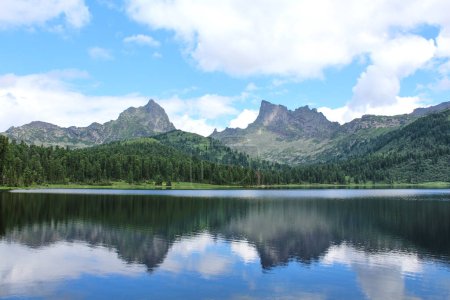 Ufer des großen Bergsees im Naturpark. Sommerlandschaft bei gutem Wetter. ruhiges Wasser und symmetrische Reflexion. Zwei hohe Gipfel und blauer Himmel mit Wolken