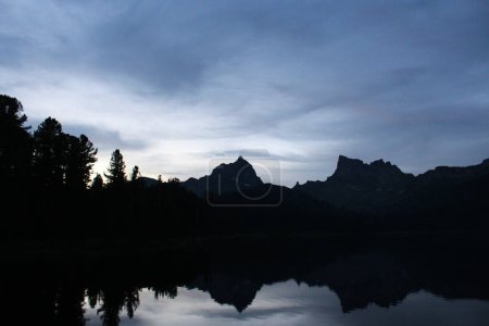 Im Wasser des Sees spiegeln sich die Silhouetten zweier felsiger Berggipfel. Naturlandschaft in der Dämmerung