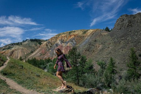 una joven vestida con un vestido corto se encuentra junto a una ruta de senderismo contra el telón de fondo del famoso hito Altai Mars en el cañón. concepto de viaje de verano