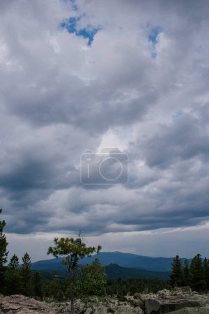 Bad weather in the mountains. gloomy dark clouds with blue gaps of clear sky. sky light. Hills, coniferous trees and stones