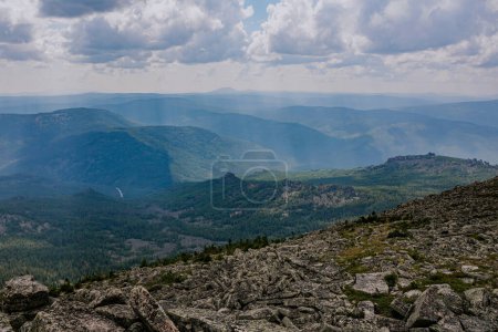 The sun's rays break through the clouds and illuminate the rocks and green forest. Natural landscape at summer day. Hike weather. Long trip in a national park in the mountains