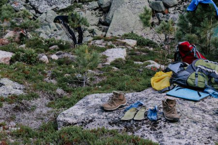 Photo for Drying equipment after a hike at the campsite. Old brown trekking boots, green insoles and blue socks to dry after day of hiking, laid out on stone. Wet feet while traveling. Travel camping - Royalty Free Image