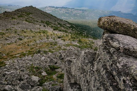 Blick von der Spitze einer Klippe auf ein Gebirgstal mit Nadelwald, Felsen und vielen Steinen. Sommerwanderung durch schwieriges Gelände