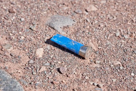 Empty blue gun casing on a dirt road out hunting grounds. Plastic sleeve for a hunting type cartridge for a smoothbore shotgun. Ammunition casings for small arms. illegal hunting and poaching