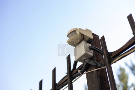 Photo for Small automatic street lamp connected to residential building communications. White flashlight with twelve diodes fixed to a metal fence outside with brightness and time adjustment. - Royalty Free Image