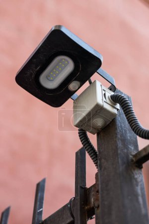 Photo for Small LED street lamp connected to residential building communications. Black flashlight with twelve diodes fixed to a metal fence outside. - Royalty Free Image