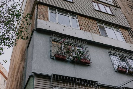 Sowjetisches mehrstöckiges Wohnhaus mit verschiedenen Balkontypen. Fenster mit Gittern und Blumen in Töpfen. Ecke eines Hauses, das während der UdSSR erbaut wurde. Verschiedene Baumaterialien. 