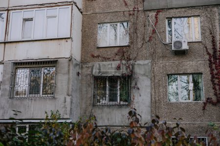 Verschiedene Arten von Balkonen und Fenstern, die in einem alten Plattenbau mit roten Efeublättern umrankt sind. Fassade sowjetisches Mehrfamilienhaus. Externe Klimaanlage hängt unter dem Fenster