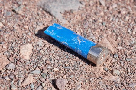 Plastic sleeve for a hunting type cartridge for a smoothbore shotgun. Ammunition casings for small arms. Empty blue gun casing on a dirt road out hunting grounds. illegal hunting and poaching