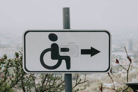 White Road sign for people with disabilities, disabled, with black icon man in wheelchair and right arrow. Accessible environment in urban space. 
