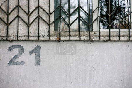 Hausnummerierung. Die Zahl 21 21 wird mit einer Schablone auf eine graue Wand unter einem Fenster mit Gittern gemalt.. 