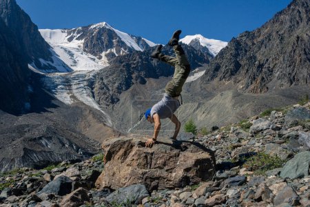 Man handstand against the background of hight mountains, snowy peaks and glacier. Sports and training in nature, outdoors on hike. Siberian power, Altai Aktru, summer mountain landscape. GO Everywhere