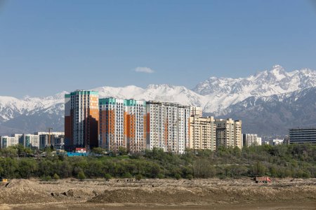 Cityscape, housing complex with best view of mountainous area. Apartment buildings against backdrop of high snow-capped mountains. Almaty, Kazakhstan. Copy space, blue sky. Unity of city and nature