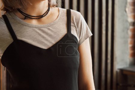 Frau mit schwarzem, dünnem Trägertop über grauem T-Shirt. Konzept: Kombination von Kleidungsstücken aus dem Kleiderschrank miteinander und Accessoire-Schmuck. Schwarze Perlen in zwei Reihen hängen am Hals