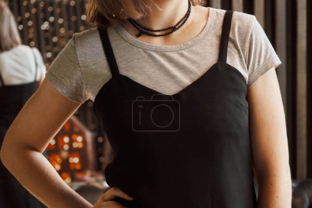Photo for Woman wearing a black thin straps dress over a gray T-shirt. Concept: Combination of clothes from the wardrobe with each other and accessory jewelry. Black beaded beads in two rows hang on the neck - Royalty Free Image