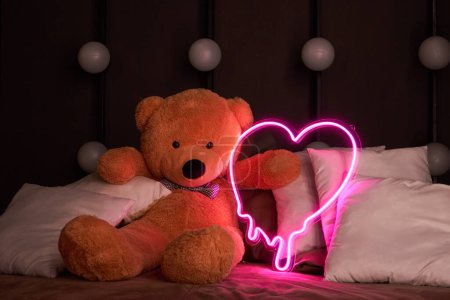 Valentinstag 14. Februar Konzept, Geschenk romantischen Hintergrund. Liebeserklärung, Glückwunsch zum Urlaub oder Jubiläum. Brauner Teddybär liegt in Kissen und hält ein neonrosa Herz. 