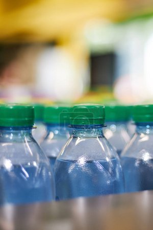 Blue plastic half-liter small volume mineral water bottles with green cap lid in store, supermarket shelf, close up. High consumption of plastic in everyday life, what pollutes the environment