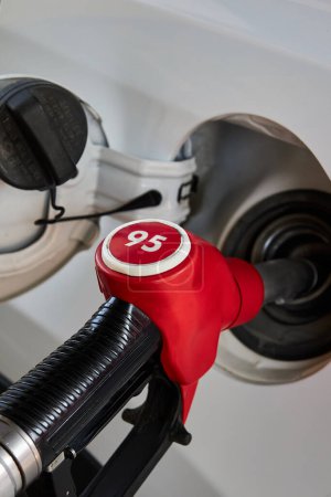 Car refueling process. Gasoline dispenser, Red fuel pump nozzle unit inserted into the gas tank of a white automobile. Refueling gun, 95 petrol benzine hose. 