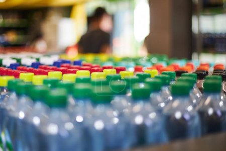 Lot of blue plastic half-liter small volume mineral water bottles, green yellow red cap in store. High consumption plastic in everyday life, what pollutes the environment. supermarket shelf, close up