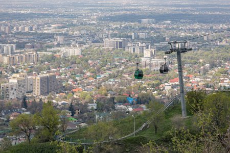 Seilbahn auf den Kok-Tobe-Hügel in Kasachstan. Seilbahn mit zwei Kabinen, vor der Kulisse der Stadt Almaty zur Frühlingszeit. Touristischer Ort, Wahrzeichen der Stadt. Stützpfeiler der Seilbahn