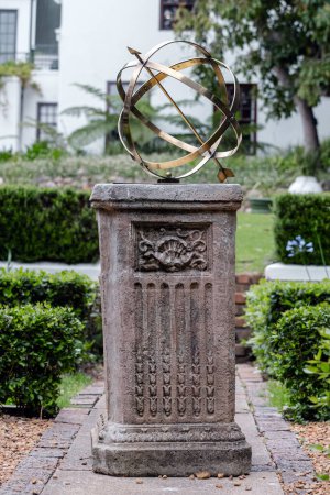 Brass or bronze large scale armillary sundial sphere with raised roman numerals and arrow directional on plinth, stone pedestal with pattern. Hotel backyard, garden