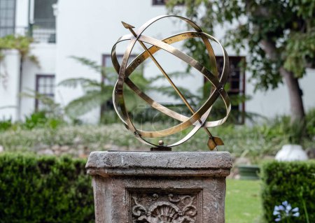 Brass or bronze large scale armillary sundial sphere with raised roman numerals and arrow directional on plinth, stone pedestal with pattern. Hotel backyard, garden