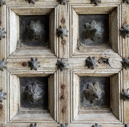 Fragment einer antiken alten Tür aus hellem, unlackiertem Holz und Metallmaterialien mit floralem Muster, Nahaufnahme. Elemente der Architektur in die Jahre gekommene Gebäude, Fensterläden