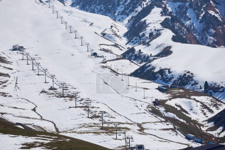 End of season, empty ski resort. Thawed patches on snowy mountain slope. Chairlifts, view from above, aerial. Winter sports activities, skiing, snowboarding. Recreation place, natural landscape travel