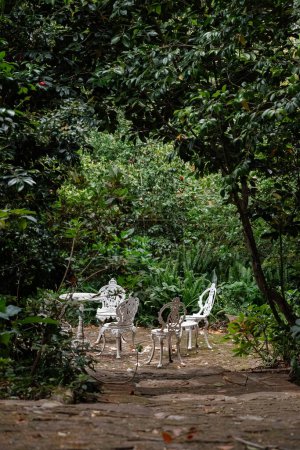 Metal outdoor furniture, vintage set. Round table and four white chairs. Lunch place in the courtyard, surrounded by trees. Relaxation area in the garden