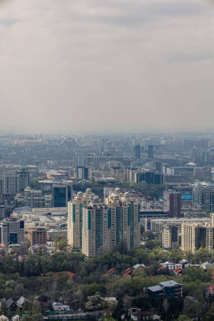Blick auf die Stadt Almaty, Republik Kasachstan, Zentralasien. Stadtbild im Frühling, Hoch- und Flachbauten, Wohngebäude, Büros und Geschäftszentren. Dunst über der Stadt. Ökologie